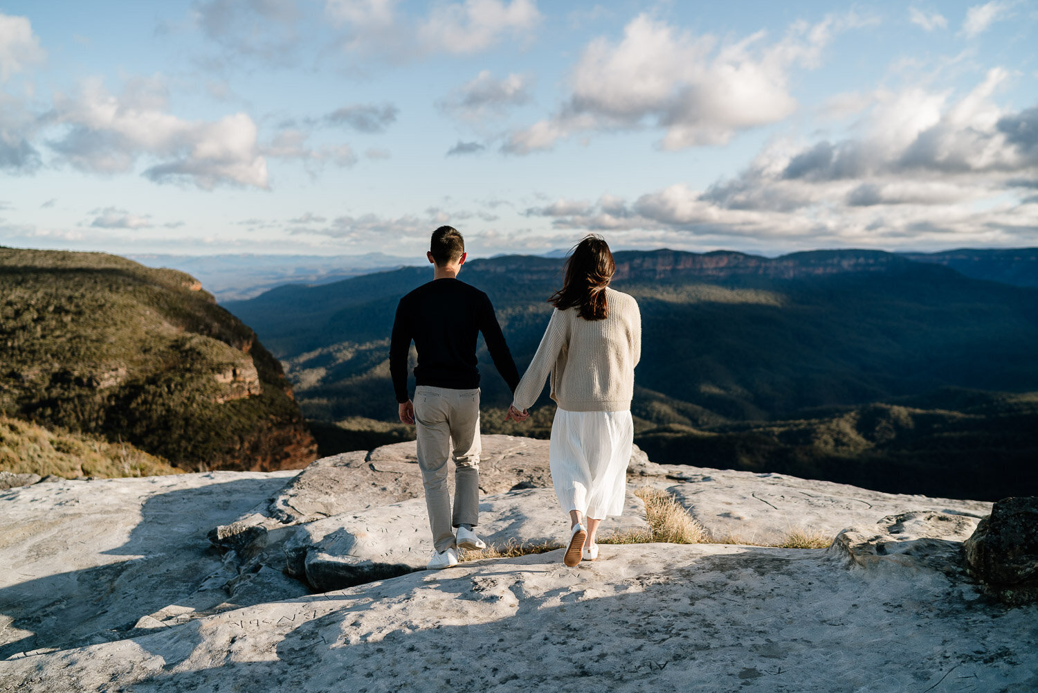 Couple standing on a clifftop above a valley at golden hour