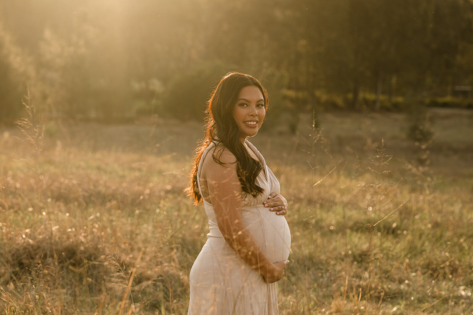 Expecting mother backlit by golden light in a Sydney field