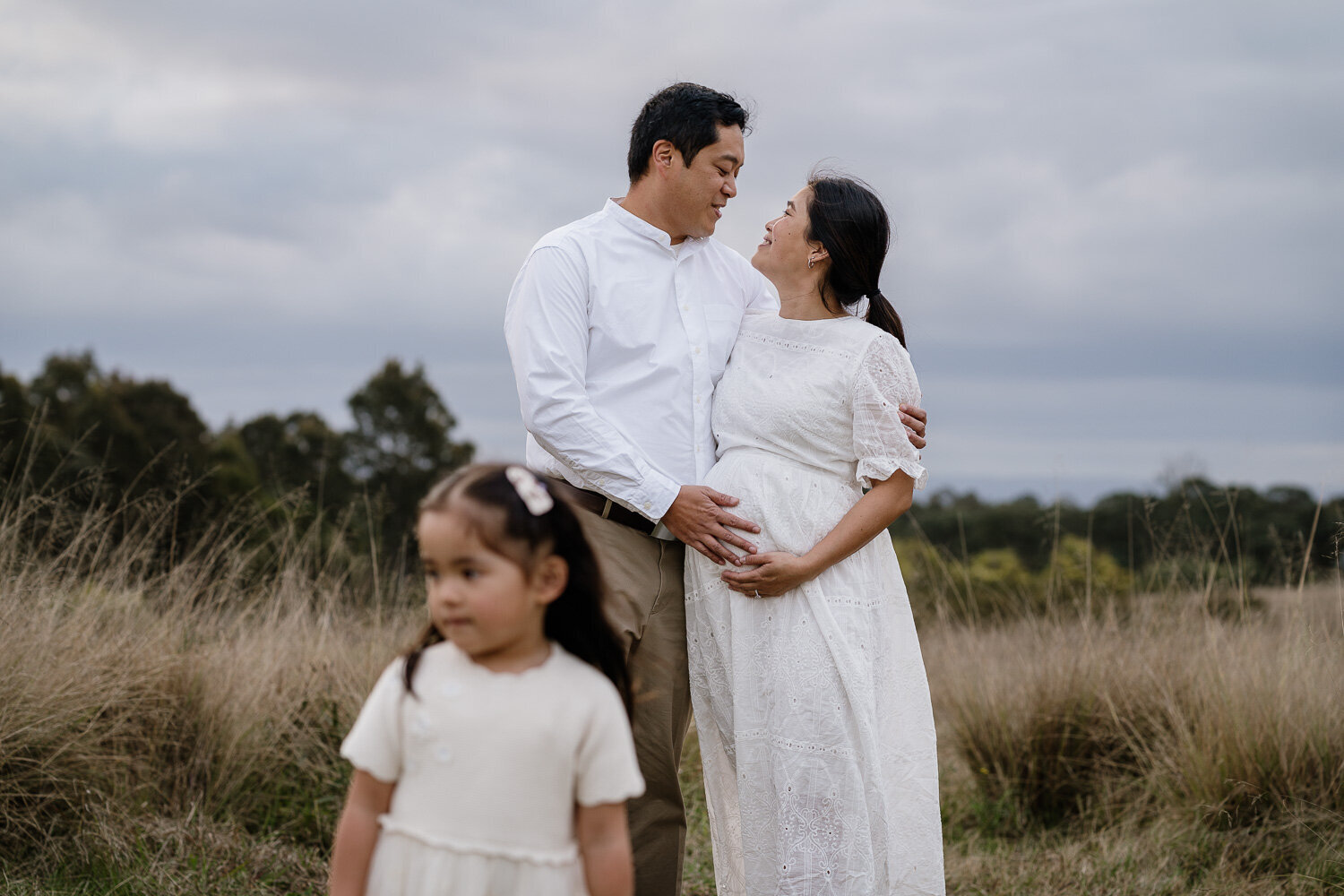 Expecting parents and their daughter in a Sydney field at golden hour